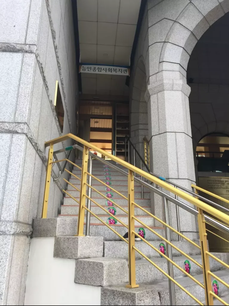 Dezelfde trap van onderaf gezien, met het Koreaanse naambord boven de ingang van het welzijnscentrum in Seoul