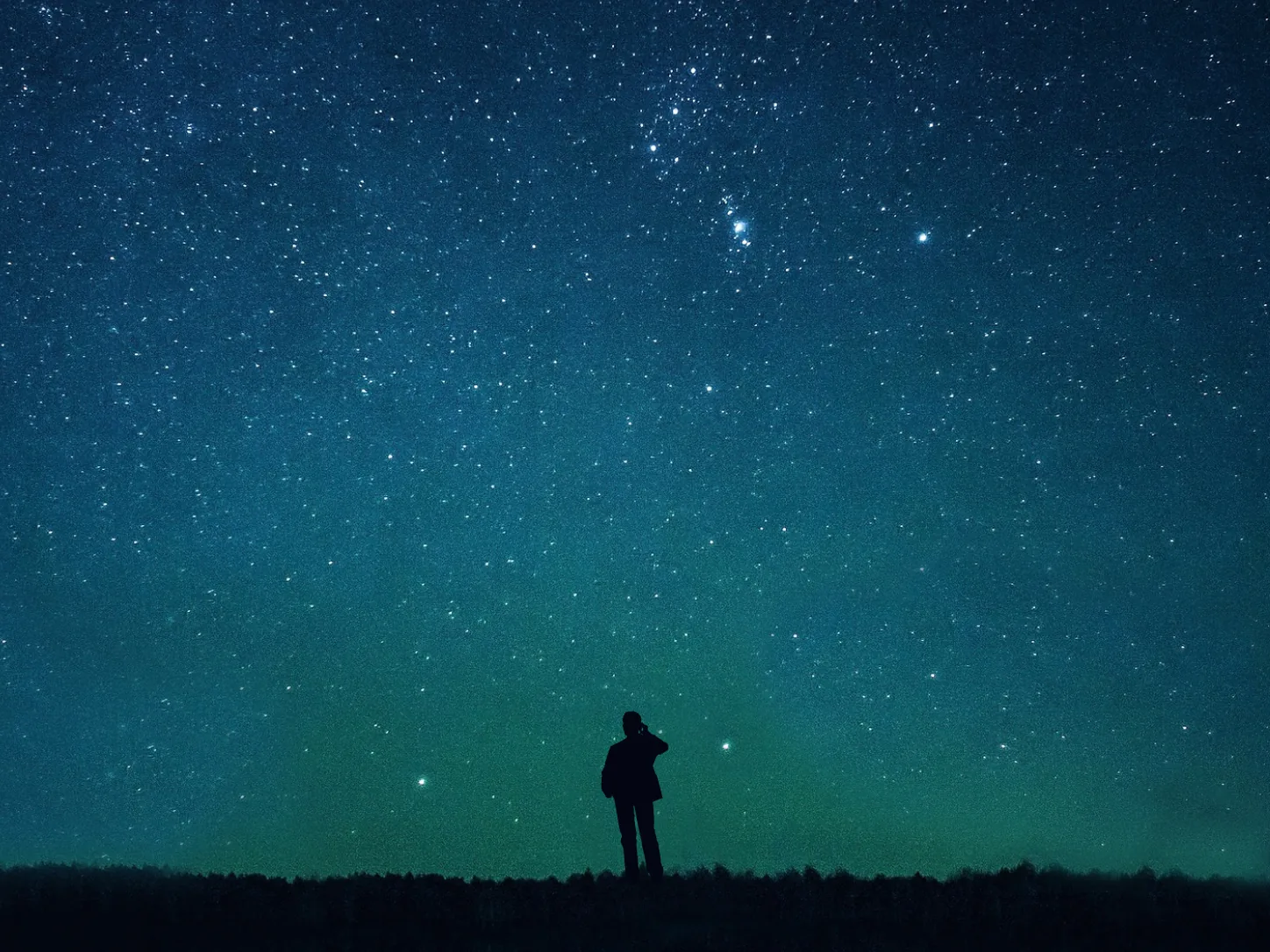 A lone figure sitting on the ground, looking up at a star-filled sky
